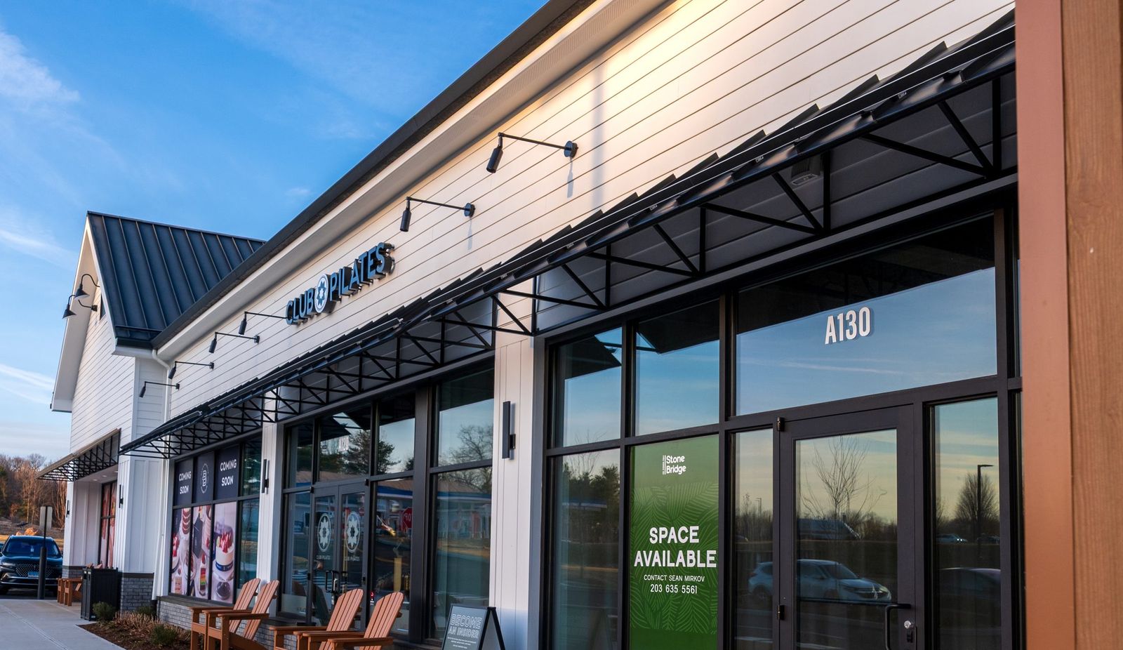 Black metal storefront awnings along a Club Pilates retail unit installed by Manchester Awning