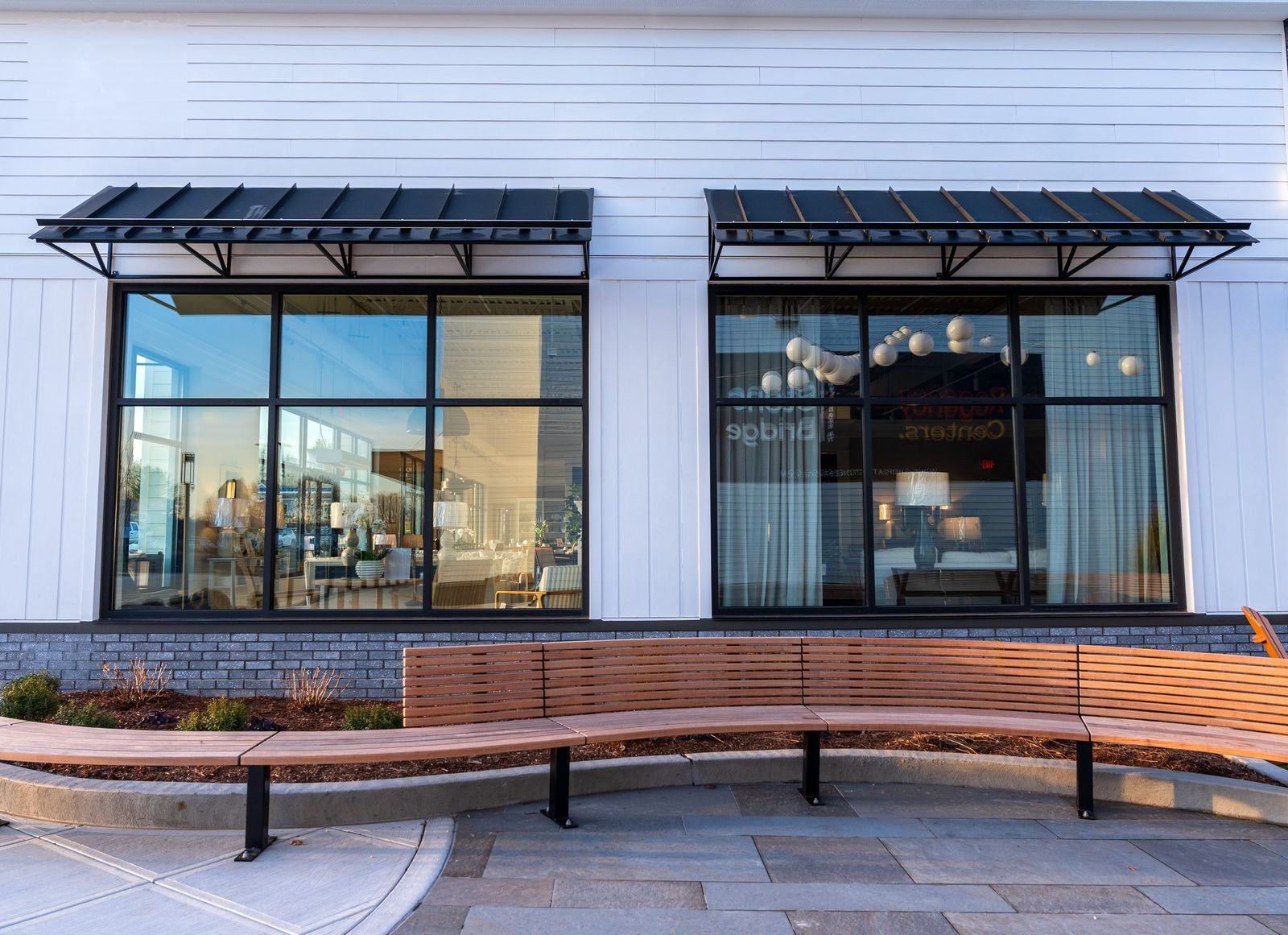 Two black metal window awnings above a curved wood bench outside a Connecticut storefront by Manchester Awning